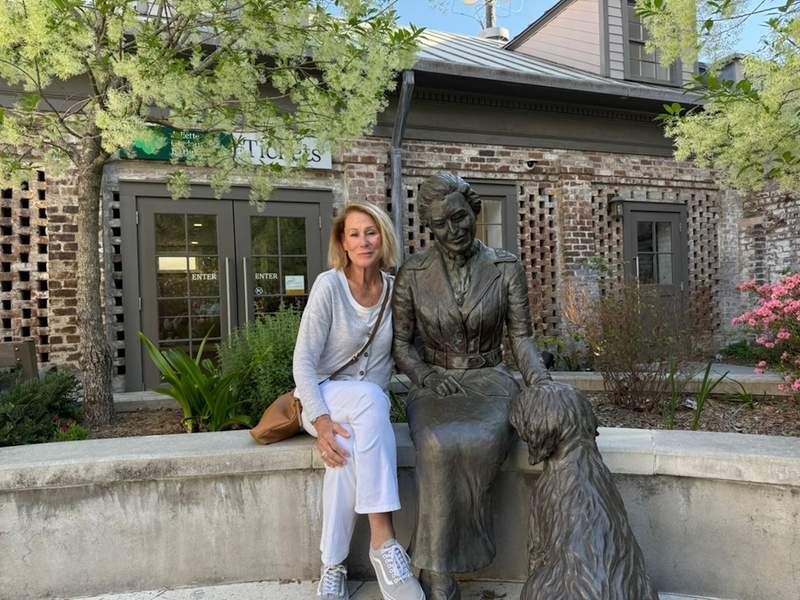 Woman sitting on a ledge with a bronze sculpture of Juliette Gordon Low and her dog Scout, Museum doors in the background. 