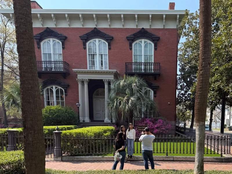 Red Brick two story period house with symmetrical windows and center door with iron fence surround with family taking photo. 