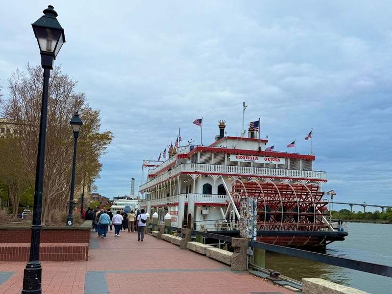 Red brick walkway beside the Savannah river and people waiting to board the paddle boat Georgia Queen 