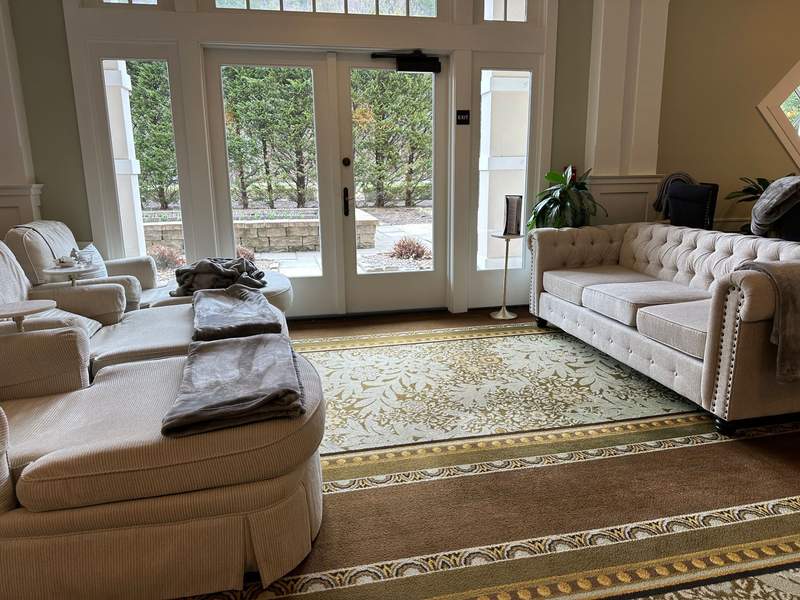 A room with a tan couch and some lounge chairs and a view of outside.