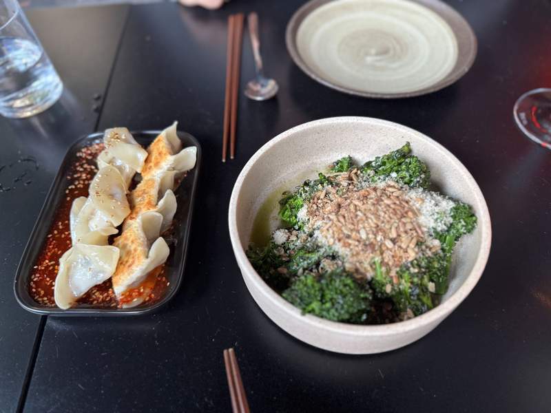 A plate of dumplings and a dish of broccoli sitting on a table at a restaurant in Adelaide.
