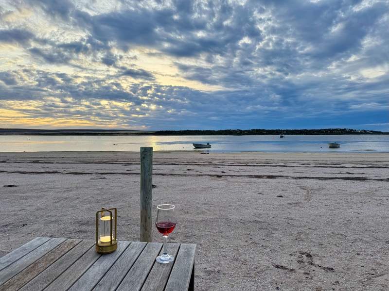 A candle and a glass of wine on a table on the beach in South Australia.