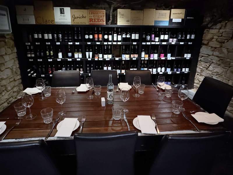A table situated in front of a wall of wine bottles in the Sevenhill Hotel wine cellar.