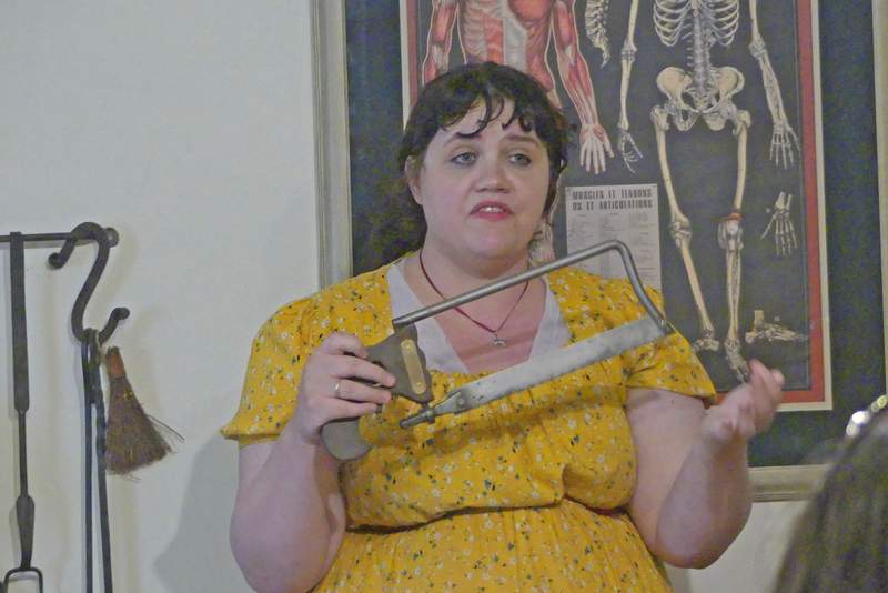A museum docent in period costume demonstrating 18th-century surgical tools and a bone saw at the Spanish Military Hospital Museum.used for amputations.