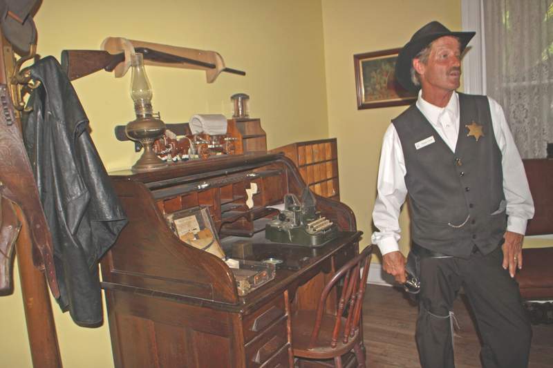 A tour guide dressed as a 19th-century deputy standing behind a wooden desk in the historic Old Jail museum in St. Augustine.