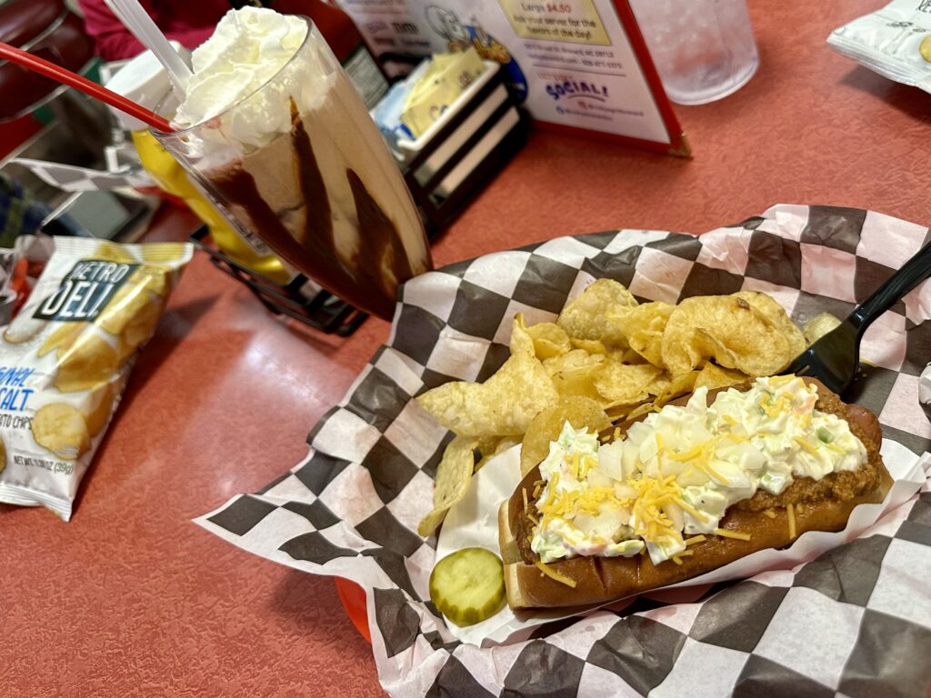 Chocolate milkshake next to black and white lined basket with chips and a hot dog at Rocky's in Brevard, NC.