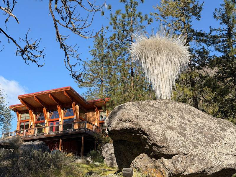 Mountain cottage with cedar siding and lots of windows. Large stone with a glass sculpture on top.