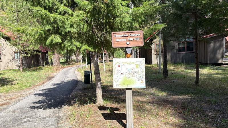 Paved path leads to two buildings, one on each side. Trees surround both, and a sign with a map of the property.
