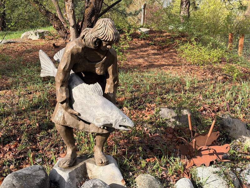 Statue of a native woman holding a salmon in a garden