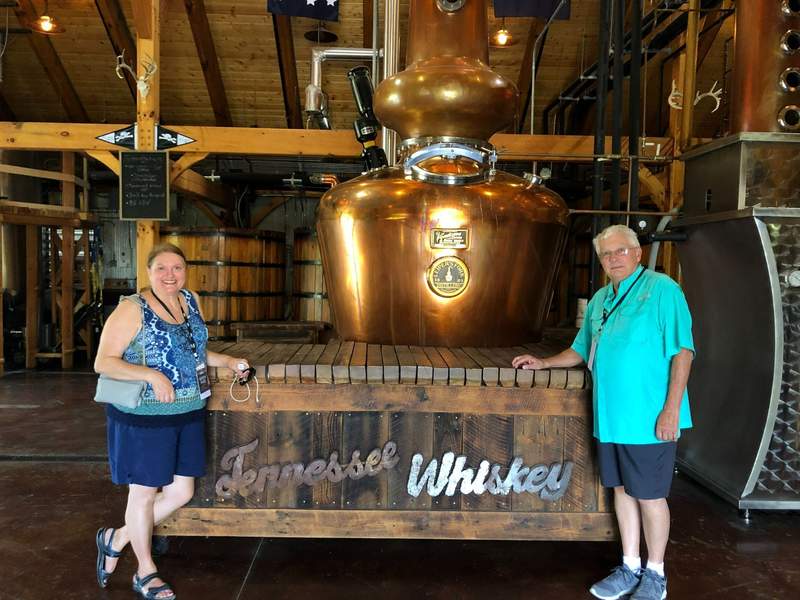 A man and woman in front of a sign that says Tennessee Whiskey.