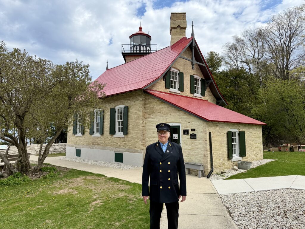 Man dressed in historic lighthouse keeper costume in front of red roofed Eagle Bluff lighthouse station in Door County Wisconsin