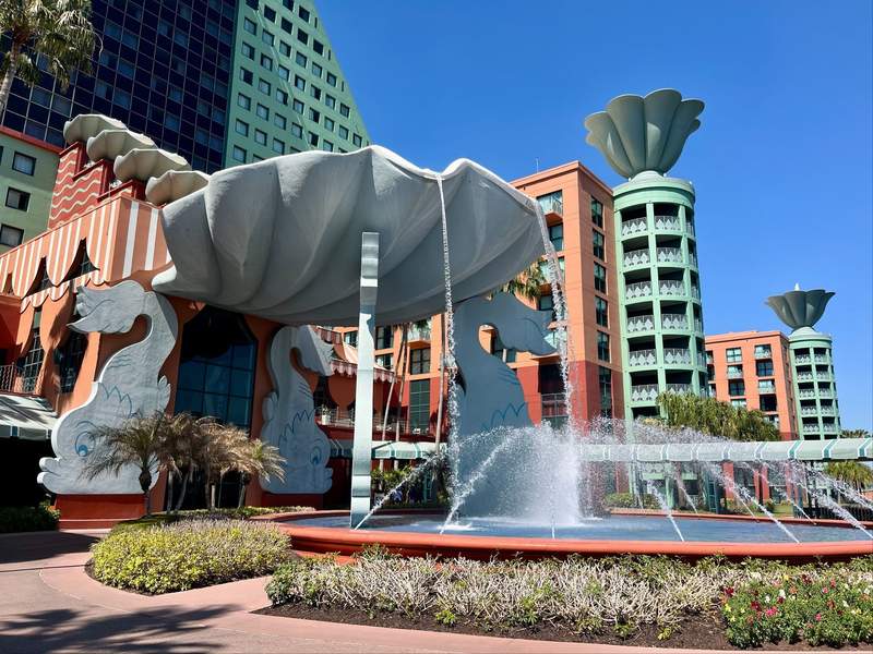 A huge decorative fountain featuring dolphins and an overturned shell is located outside the turquoise and coral exterior of the Dolphin hotel.