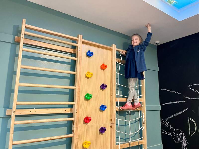 A young girl stands at the top of a kid-sized climbing wall inside the Camp Dolphin kids club at the Dolphin hotel. 