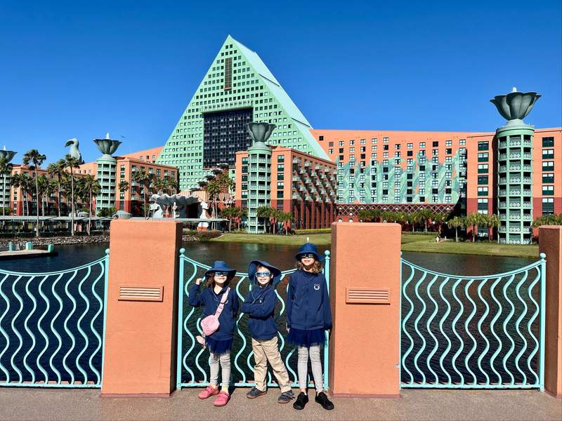Three children stand on the bridge in front of the turquoise and coral exterior of the Dolphin hotel. 