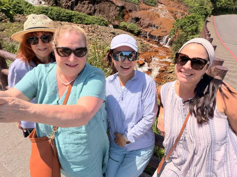 Four happy women take their photo in front of a rocky waterfall.