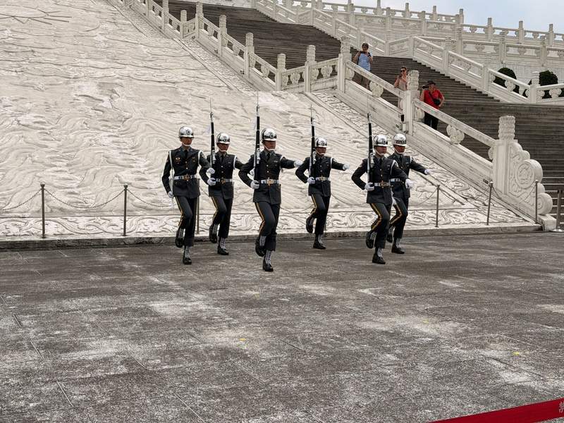 Six soldiers with silver helmets and rifles drill in front of white marble stairs.