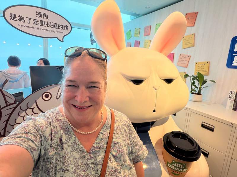 Lady takes a selfie at a photo op with a large cartoon rabbit behind her and the windows looking out from Taipei 101.