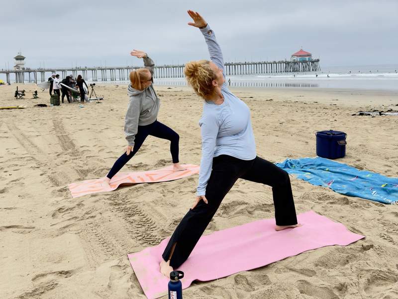 Kim Orlando and friend in warrior pose overlooking the ocean and the Huntington Beach pier.