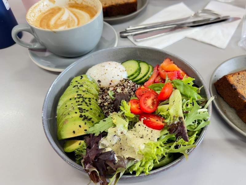 Vibrant greens with avocado tomato cucumbers and a cup of coffee with a foam top at 1oz Coffee in Huntington Beach.
