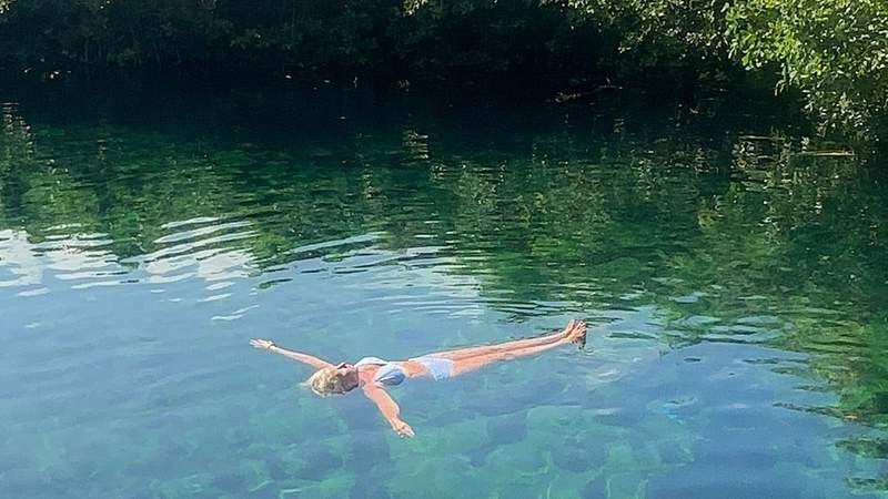 Woman floating in a clear cenote surrounded by jungle at Sandos Caracol Nature Resort in Playa del Carmen Mexico.