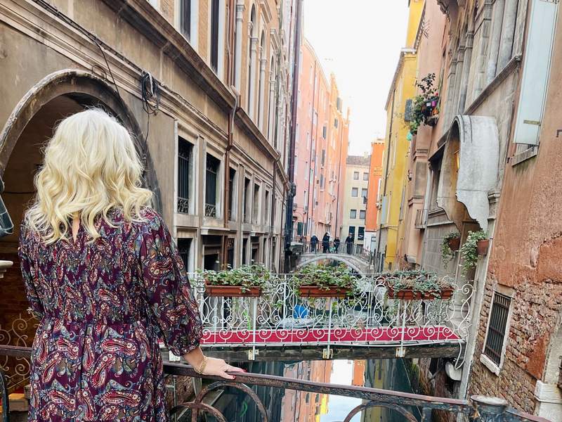 woman standing on bridge overlooking canals in Venice, Italy. 