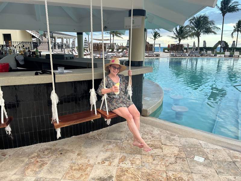 Woman sitting by the pool bar holding a frosty glass with a tropical pina colada.