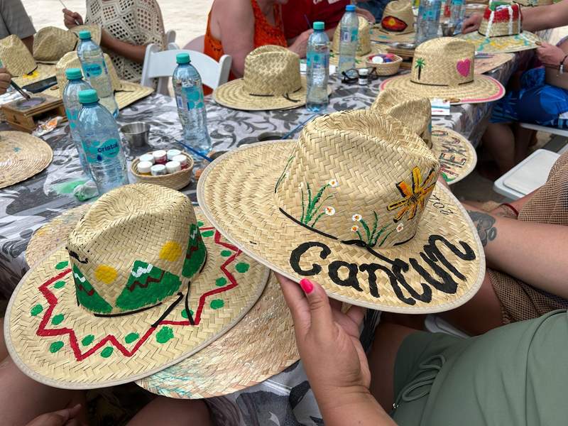 Two straw hats painted by guests; one with an abstract design and the other with flowers and the word “Cancun.”