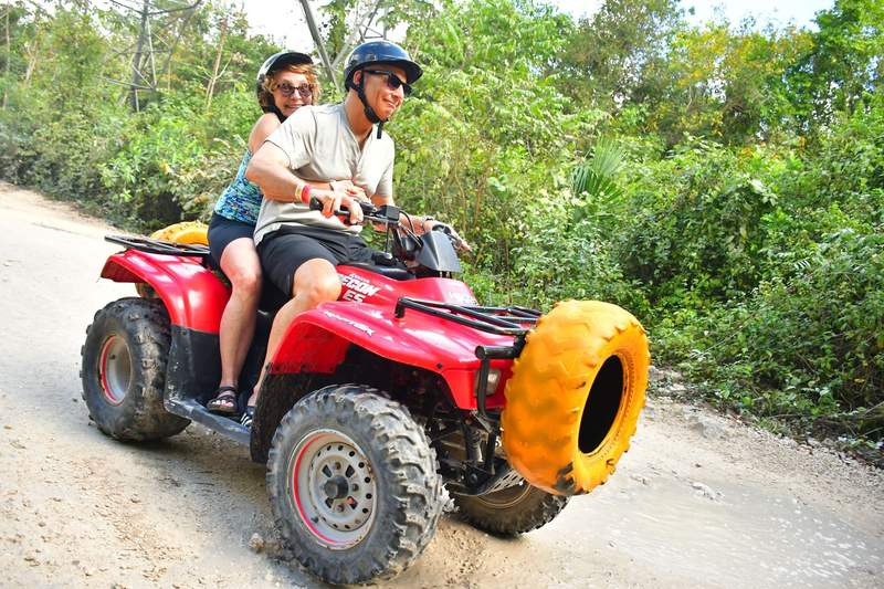 A man driving a red ATV with bright yellow tire, while a woman holds on to him in the back.