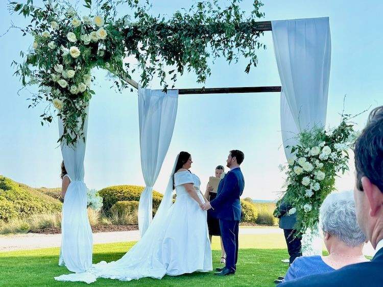 Bride and groom beneath a wedding arbor adorned with flowers and vines.