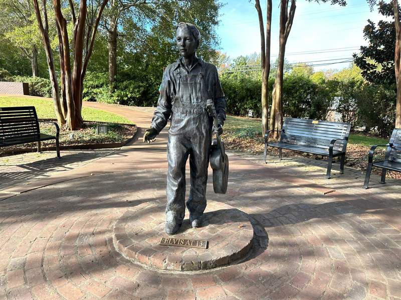 Bronze statue of a young Elvis Presley carrying a guitar.
