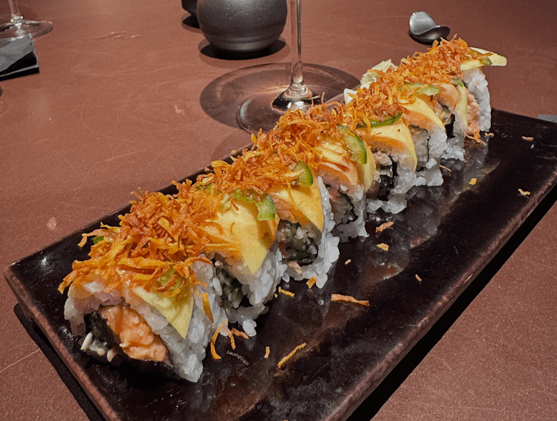 Aruba Roll specialty sushi with spicy salmon mango and crispy sweet potato on a dark plate at ShinSen Aruba