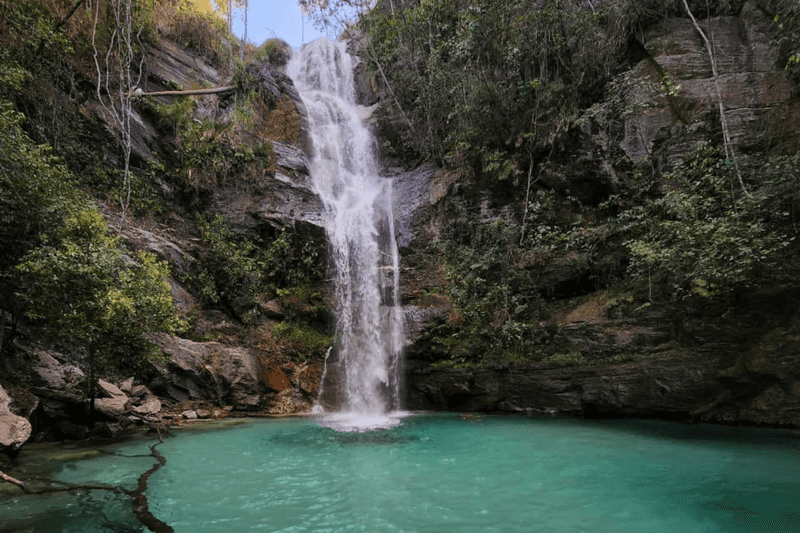 Front view of the Santa Barbara Waterfall in Chapada dos Veadeiros, with gentle waterfall falling into turquoise water, surrounded by stone walls and native green vegetation.