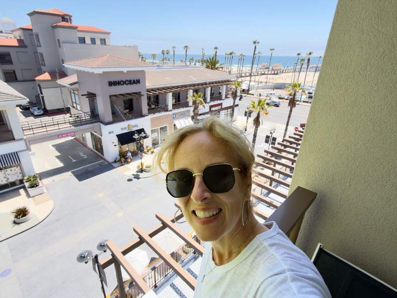 SheBuysTravel founder Kim Orlando selfie on the hotel balcony with a view of the beach and pier in the background.