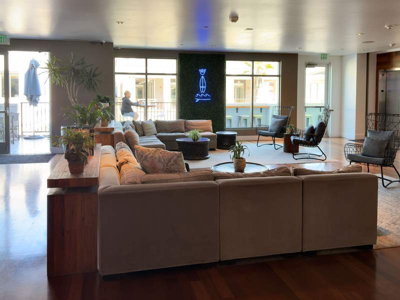 Lobby with pit couch facing sunlit windows and neon sign.