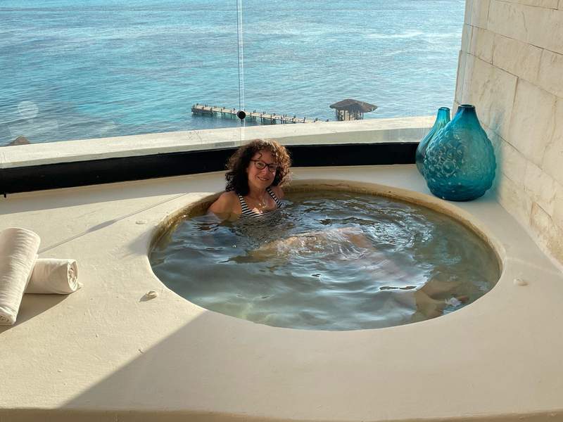 Round hot tub with woman smiling, with a view of the pier and the Blue-Green Caribbean Basin.