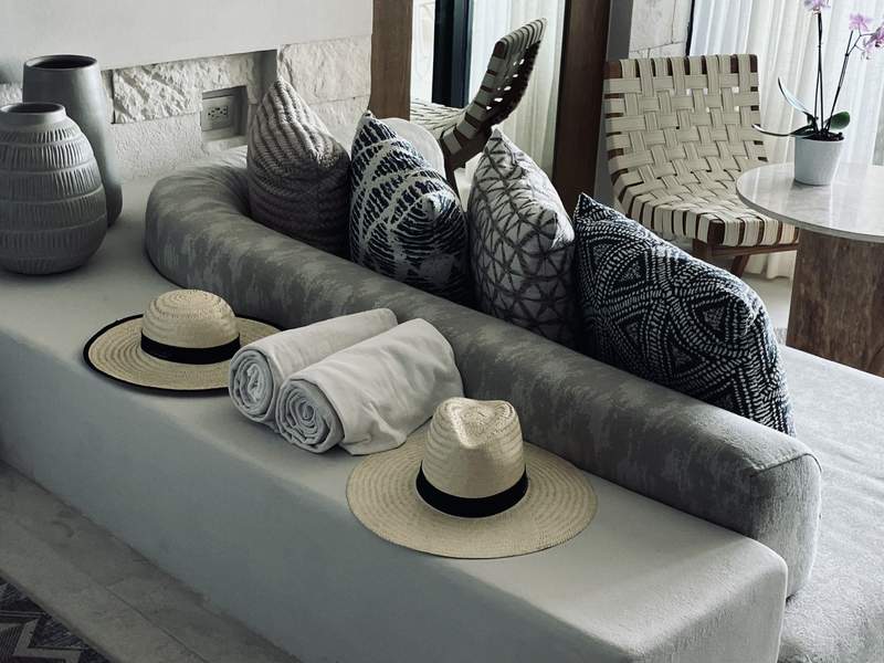 Two straw Panama hats and large plush towels sit behind a couch in the grey, black and white seating area of our suite. 