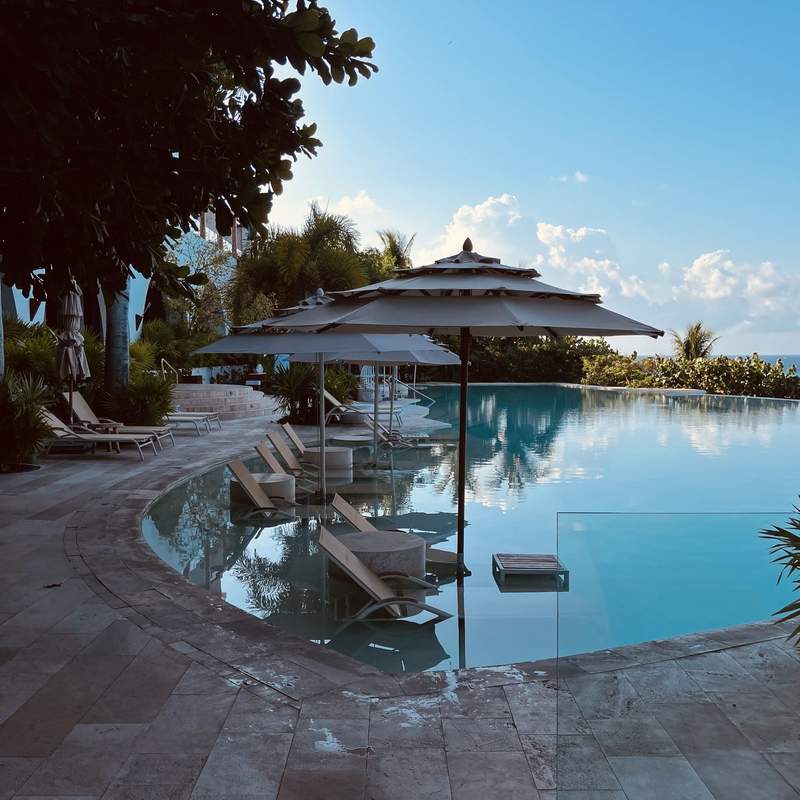 Lounge chairs and umbrellas for two sit in a large pool as the late afternoon light reflects off the water.