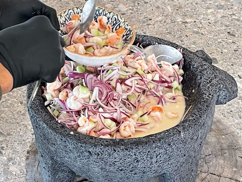 A large black molcajete made of volcanic stone, with three short legs and ceviche with shrimp, red onions and celery at the GM’s Table food demonstration.