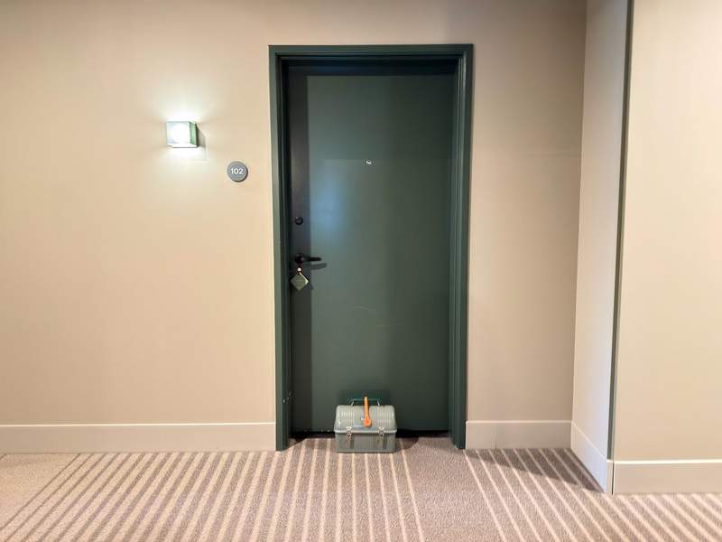 A vintage-style metal lunchbox containing a Stanley thermos of hot coffee, cream, and cups, delivered to a guest room doorstep at The Stonebreaker Hotel.