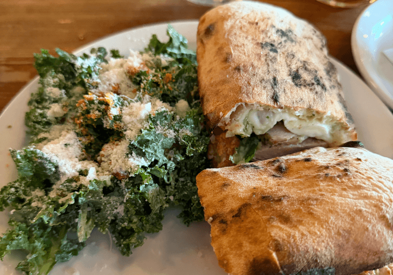 Fresh kale salad with parmesean and pollo pomodoro sandwhich on a white plate.