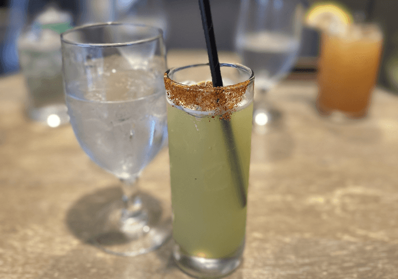 Green citrus cocktail with spiced chili salt rim and black straw in a tall glass at Dread River in Birmingham, Alabama.
