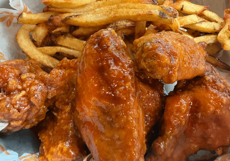 Saucy Buffalo chicken wings with seasoned French fries in a basket at Yo Mama's in Birmingham, Alabama