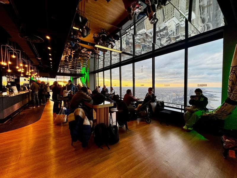 Interior view of CloudBar at the 360 CHICAGO Observation Deck on the 94th floor, with floor-to-ceiling windows overlooking sweeping panoramic views of the Chicago skyline and Lake Michigan.