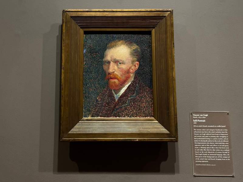 Vincent van Goghs self-portrait on display at the Art Institute of Chicago with him in a blue jacket against a swirling blue-green background.