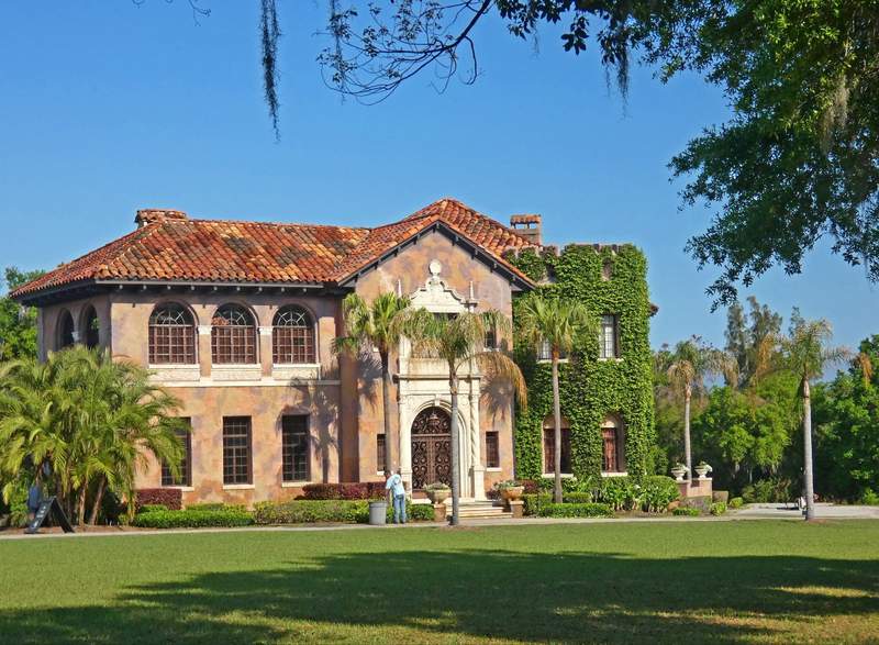 A Mediterranean Revival mansion with ivy growing on one side wall and a lawn in front.