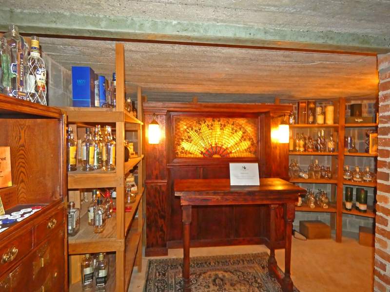A well stocked small bar with a wooden table and a glowing golden glass in a dark wood backdrop.