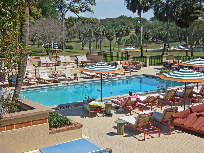 A large swimming pool with people lounging in pool chairs with umbrellas around it.