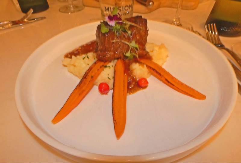 A larg portion of short rib plated on mashed potatoes with carrot strips arranged in front.
