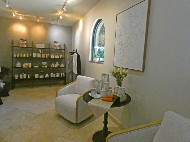 A room with two arm chairs and a row of shelves with beauty products.
