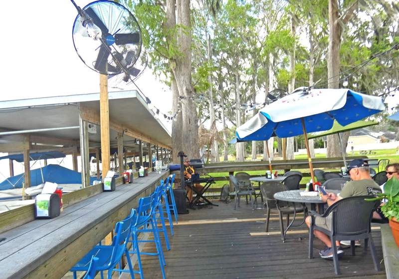 A couple sitting at an outdoor restaurant overlooking a lake with a musician in the background.